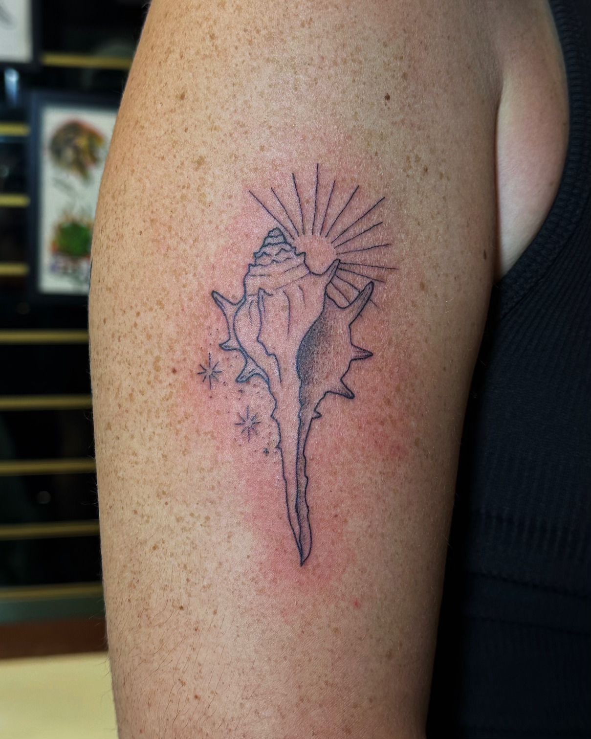 Black and grey fine line shell tattoo on upper arm