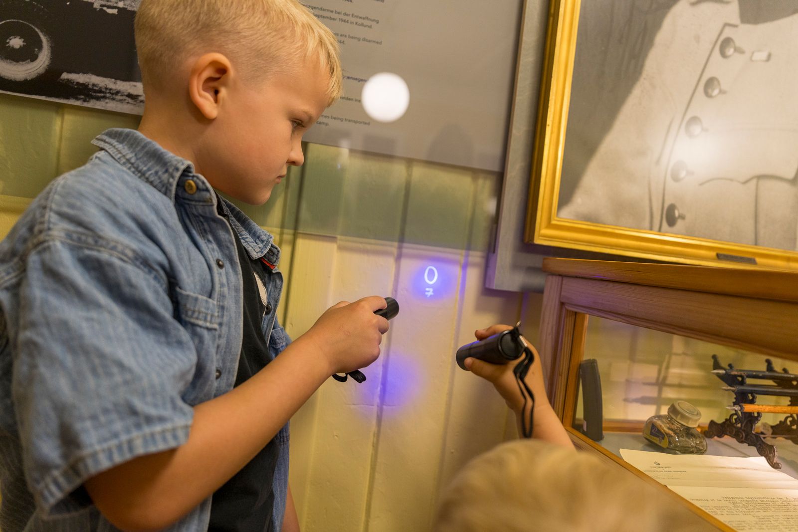Boy uses UV lamp to reveal secret message on wall in connection with the Illegal Tasks activity at Frøslev Camp.