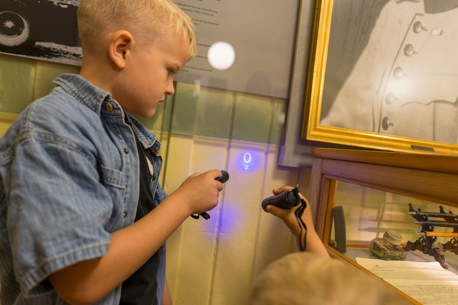 Boy uses UV lamp to reveal secret message on wall in connection with the Illegal Tasks activity at Frøslev Camp.
