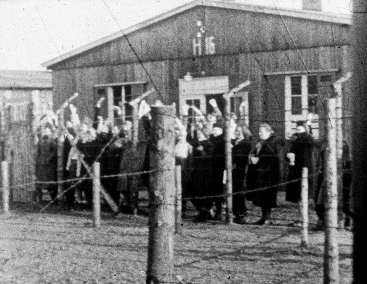 En gruppe kvindelige fanger i Frøslevlejren kigger gennem pigtrådshegnet