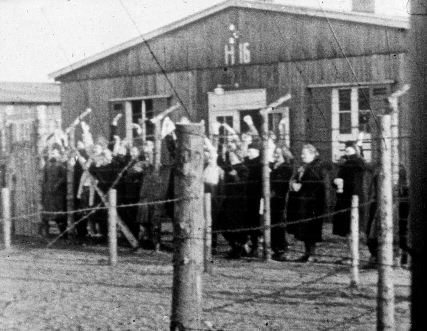 En gruppe kvindelige fanger i Frøslevlejren kigger gennem pigtrådshegnet