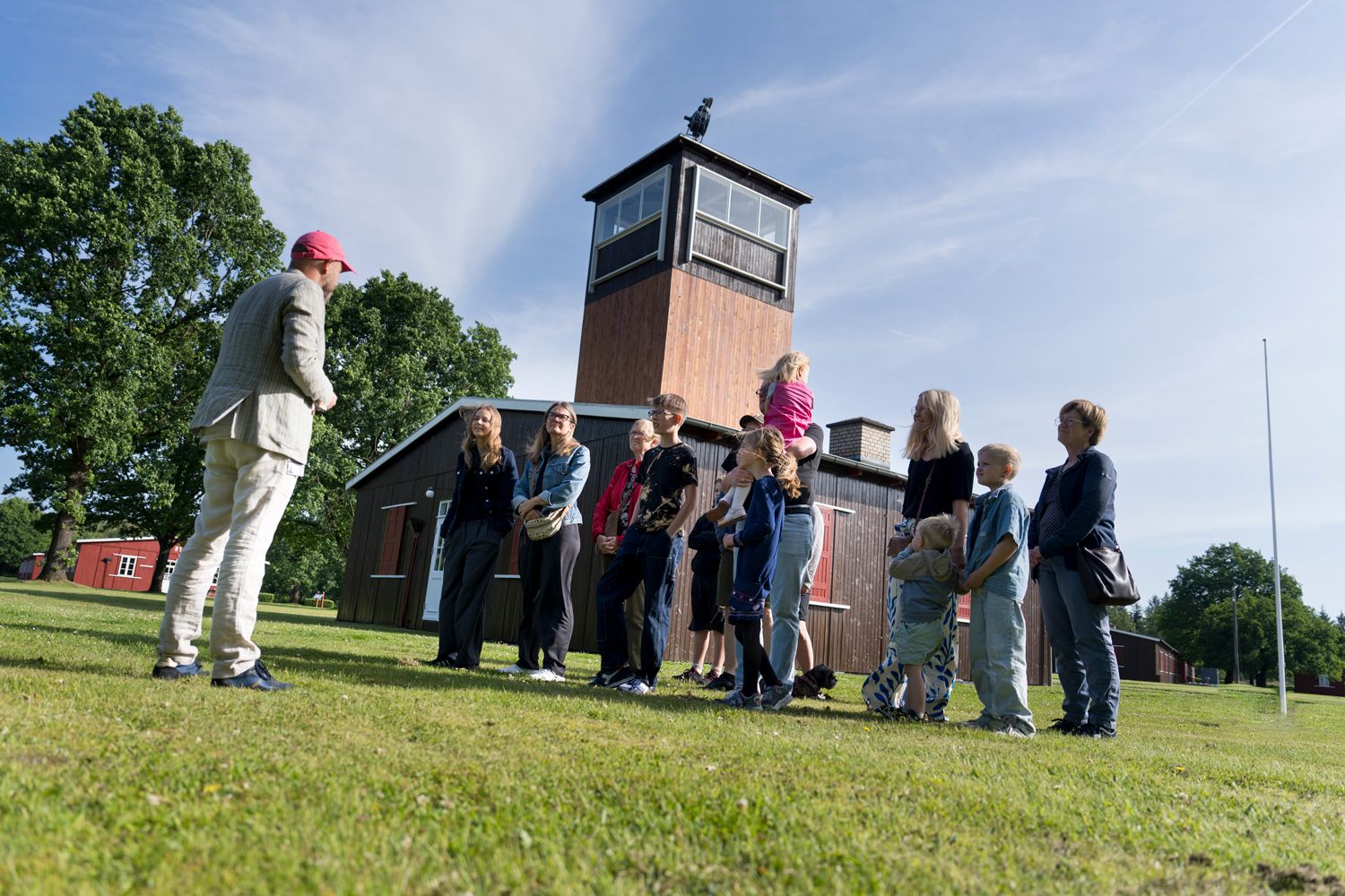 A group of people on a guided tour stand in front of the main guard tower at Frøslev Camp.