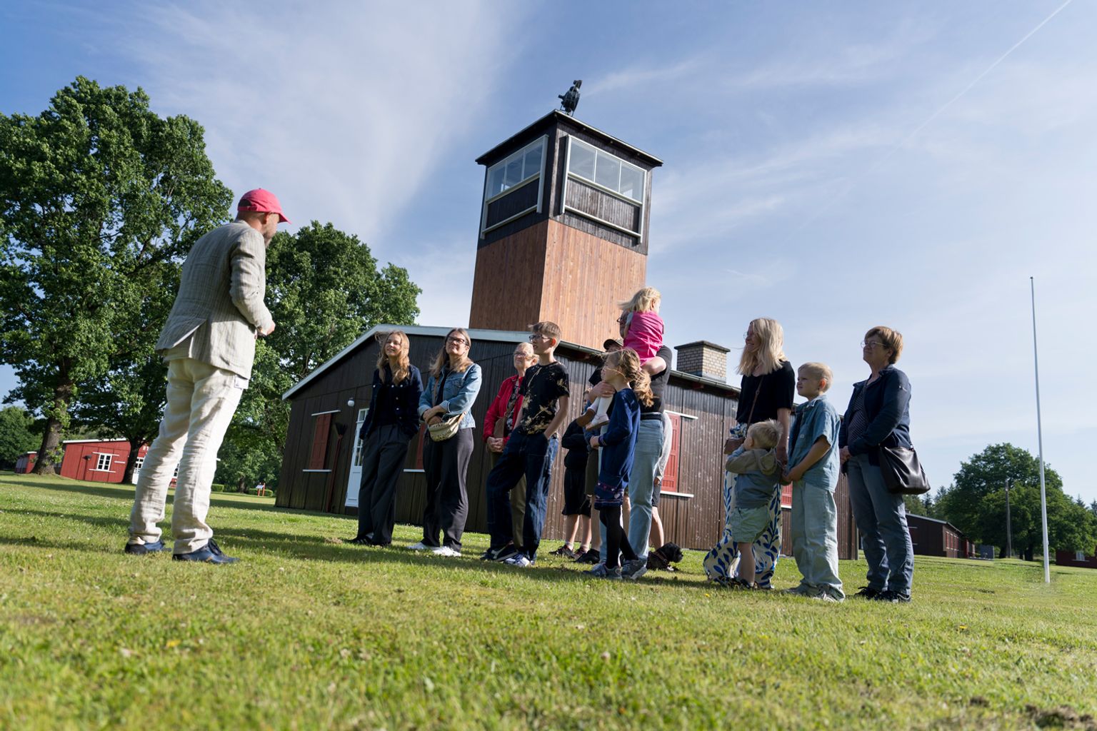 A group of people on a guided tour stand in front of the main guard tower at Frøslev Camp.