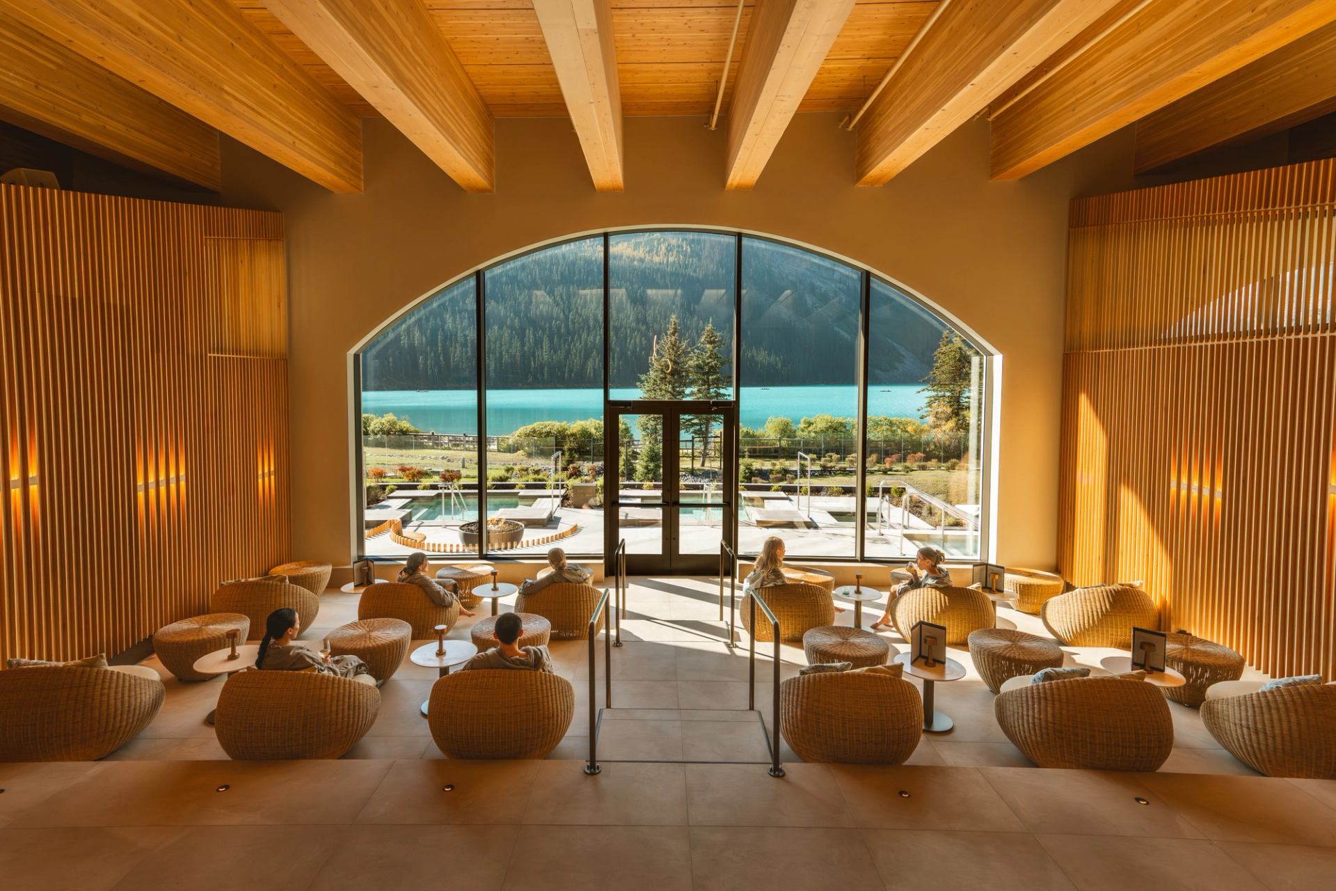 Spa-goers relax in a wood-paneled room with a large window facing Lake Louise. 