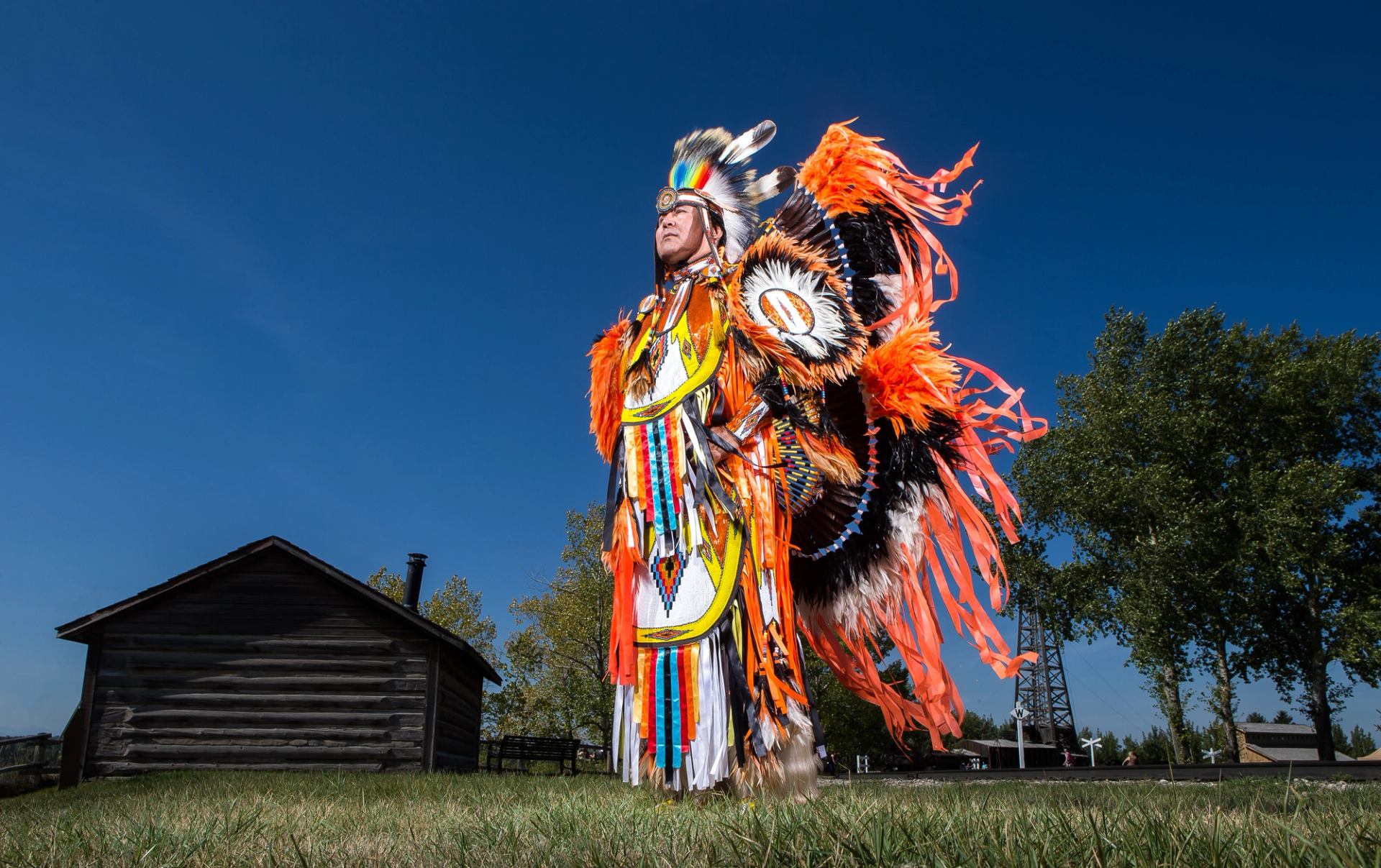 An Indigenous person in regalia stands outdoors.