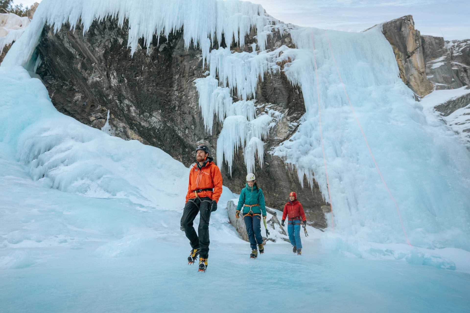 A group of ice climbers walk along the ice with frozen waterfalls behind them while ice climbing in Nordegg.