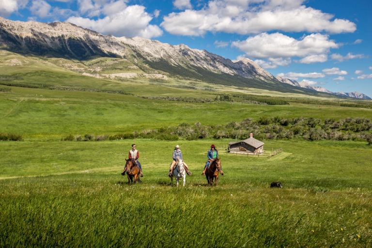 Guests ride horses through Alberta’s Foothills with mountains in the distance.