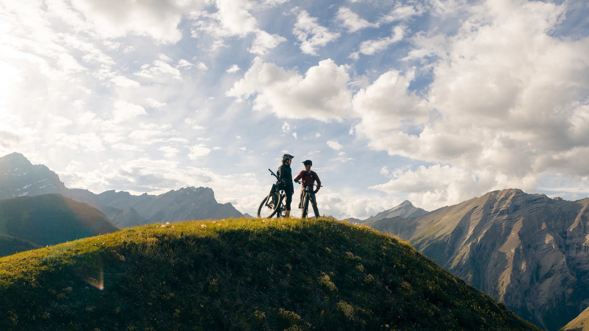 Mountain bikers pause on a grassy summit in the Canadian Rockies.