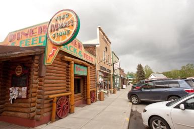 Maggie's Feed Store log building fronts a downtown street lined with shops and parked cars.