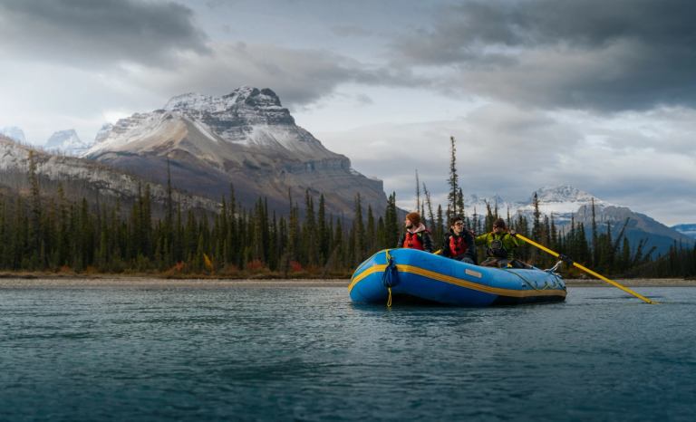 A group paddles a raft on gentle water in the Rocky Mountains.
