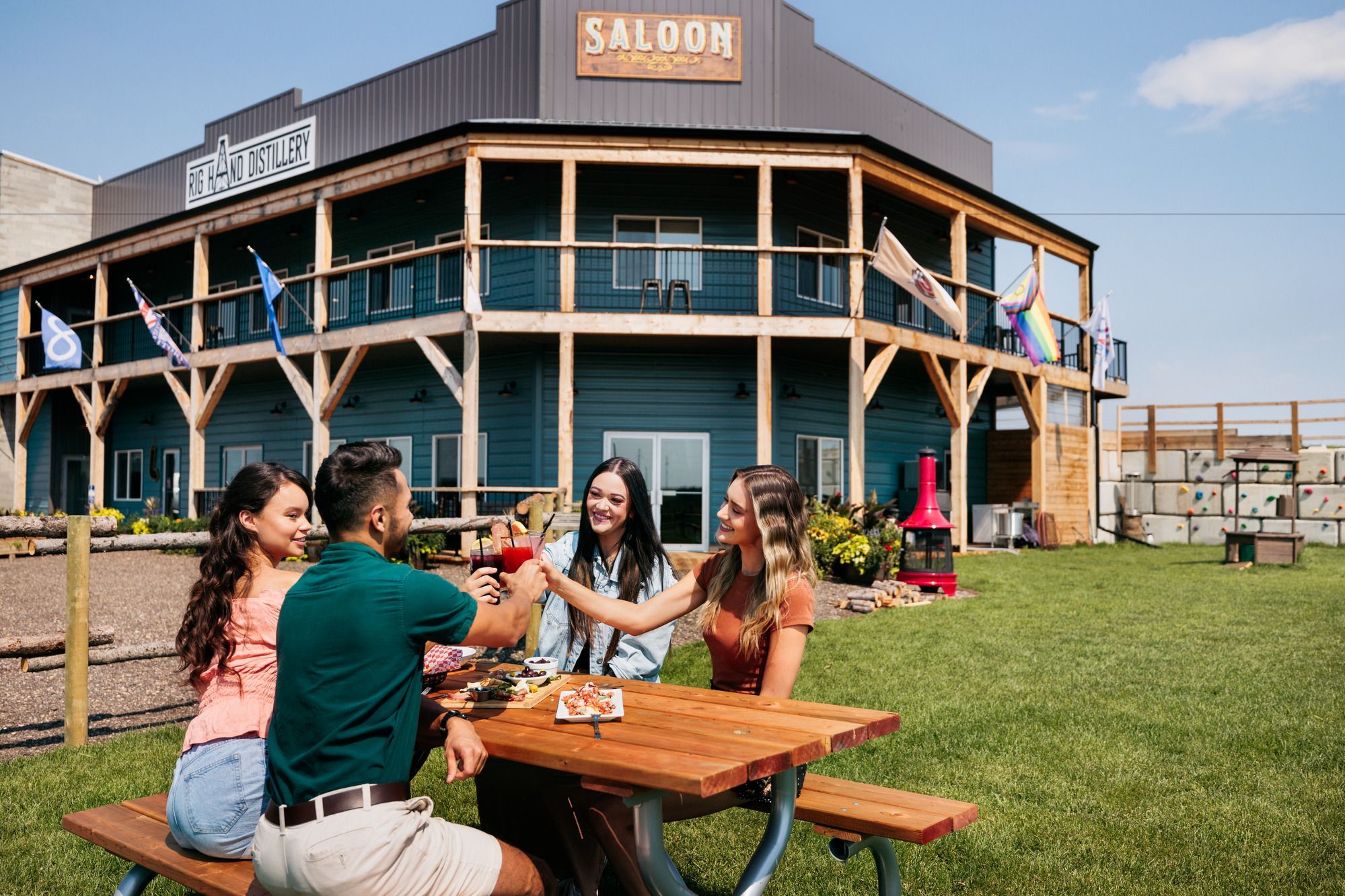 Four people cheers beverages while sitting at a picnic table outside of Rig Hand Distillery
