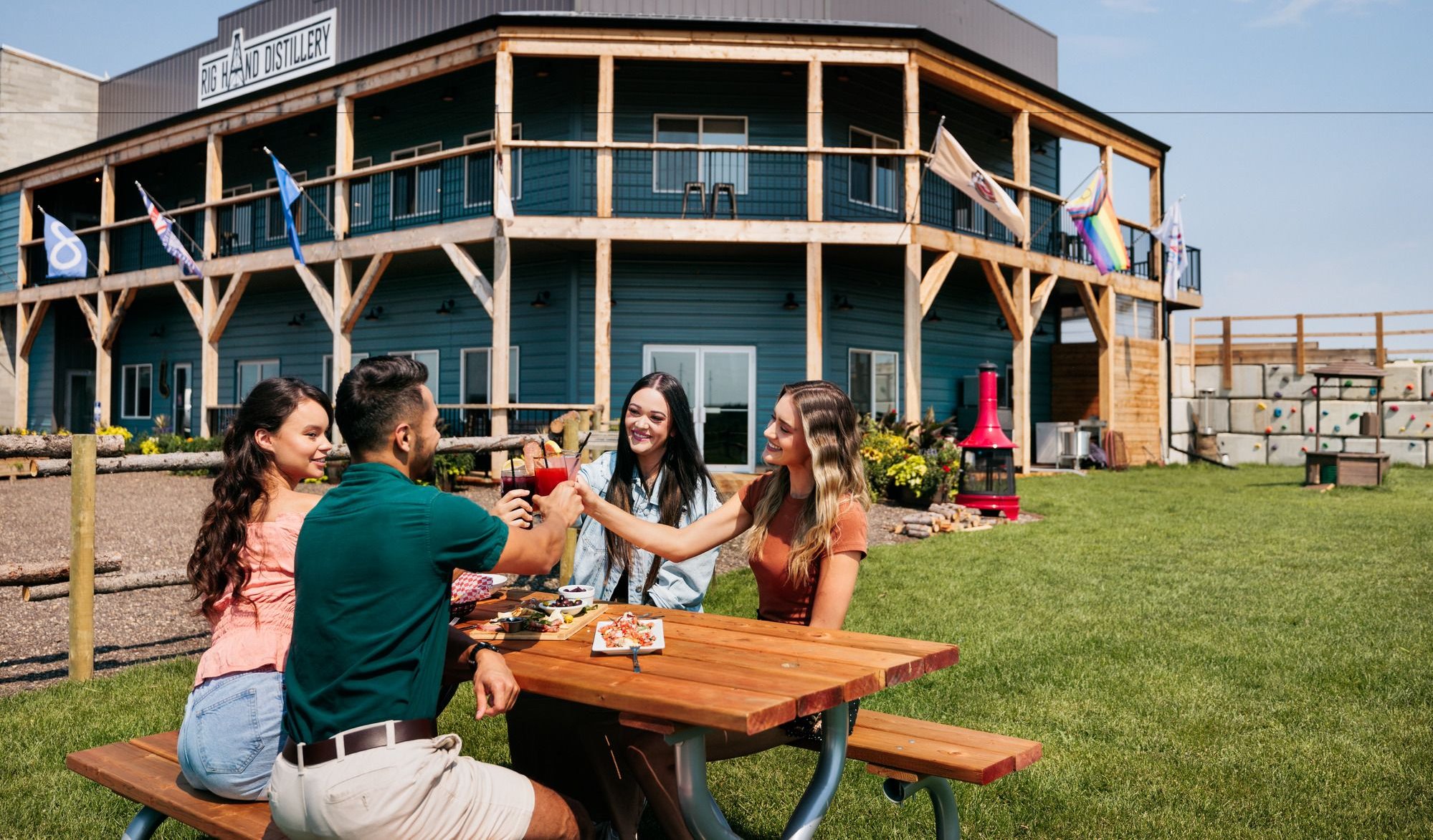 Four people cheers beverages while sitting at a picnic table outside of Rig Hand Distillery