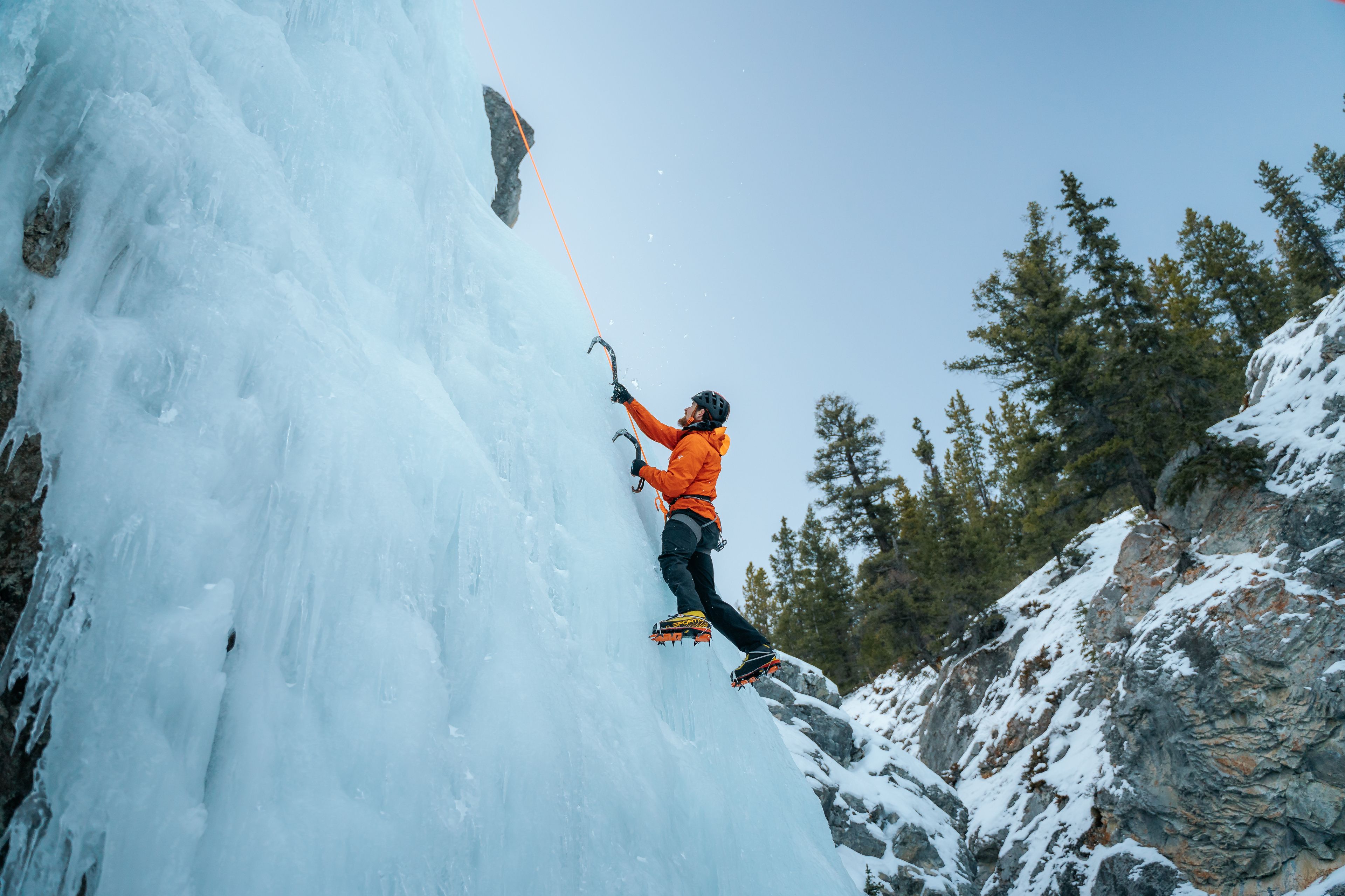 An ice climber tethered in and using ice picks to climb an ice wall in Nordegg