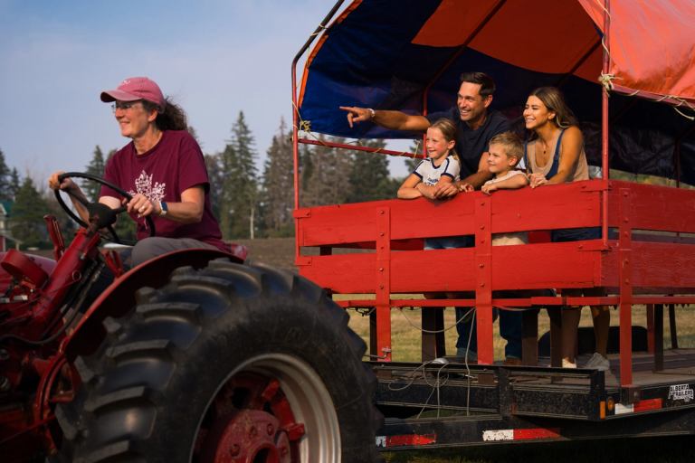 A family rides in a wagon pulled by a tractor.