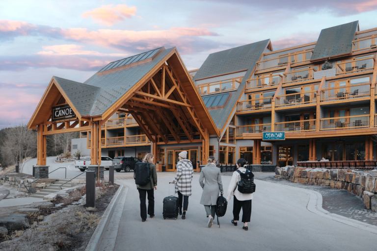 Four people walking up to the Canoe Hotel with backpacks and suitcases