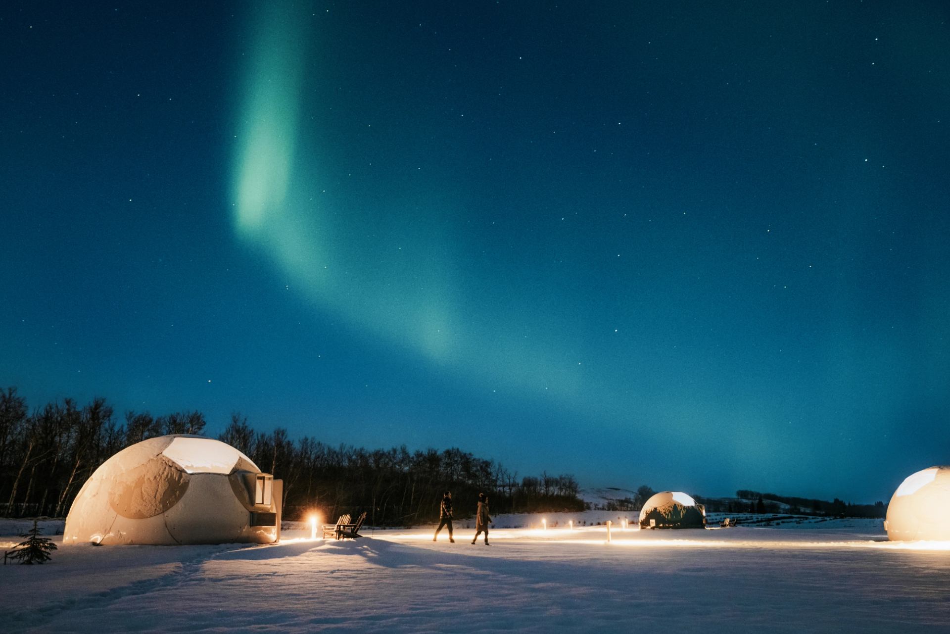 Couple walking between glamping domes with green aurora above in the night sky.