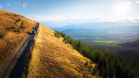 ATVs drive up a hill with forests and foothills stretching in the distance.