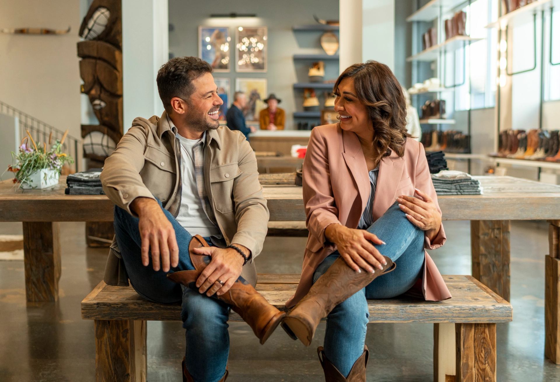 Happy couple sitting on bench trying on boots together.