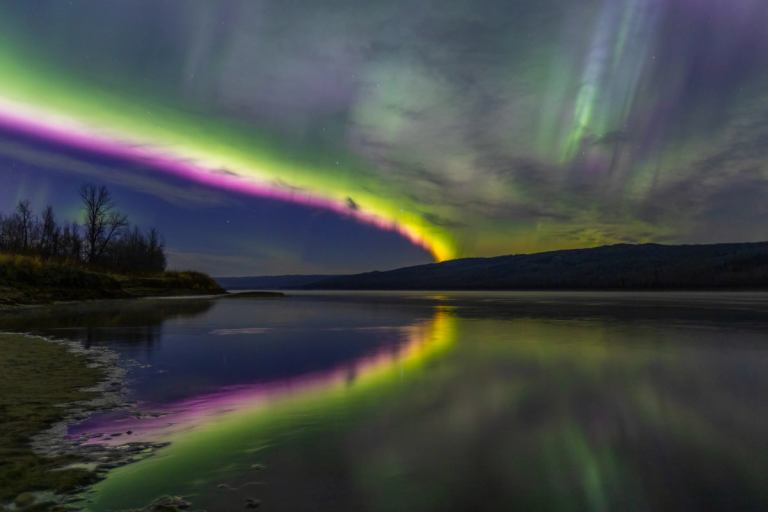A bold streak of green and pink northern lights stretch over a lake near Peace River.