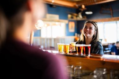 A patron picks up a beer from her flight of beers in Oldman River Brewing’s tasting room.