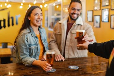 Guests take beer pints from a server in a yellow tasting room.