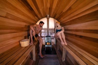 Two people relax in a barrel sauna with a view outside.