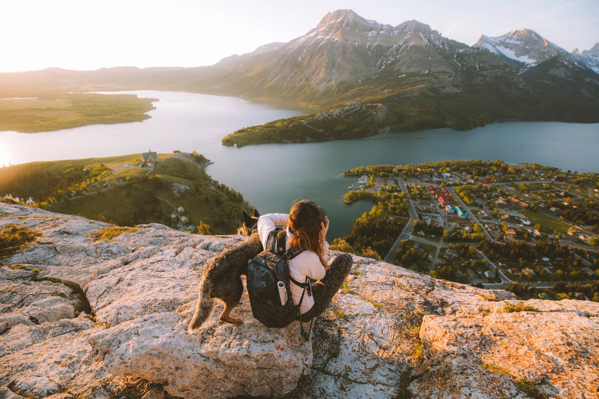 A woman and her dog sitting on rocks overlooking a town and lake below