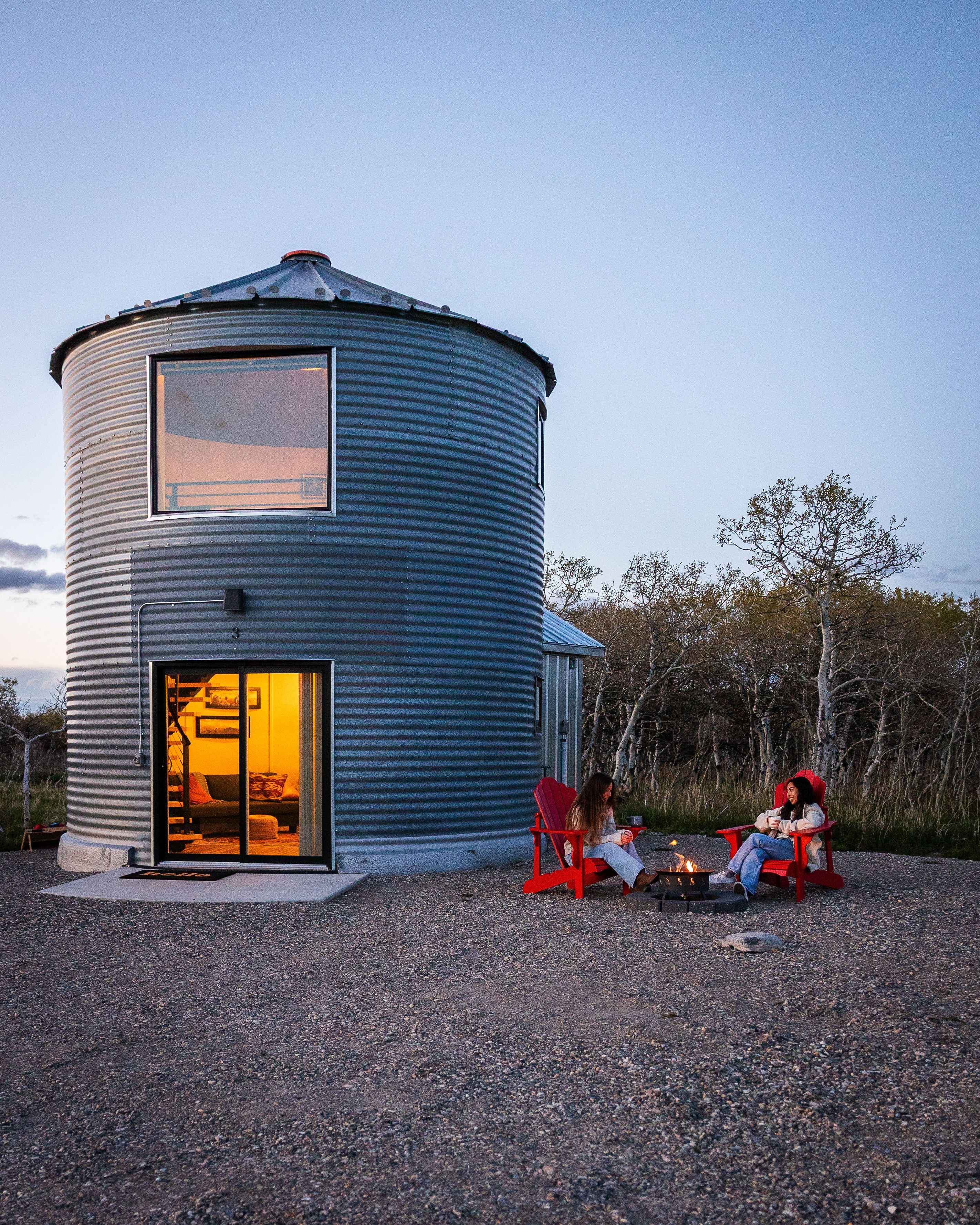 Two women sit around a firepit outside a grain silo hotel room at Twin Butte Silos.
