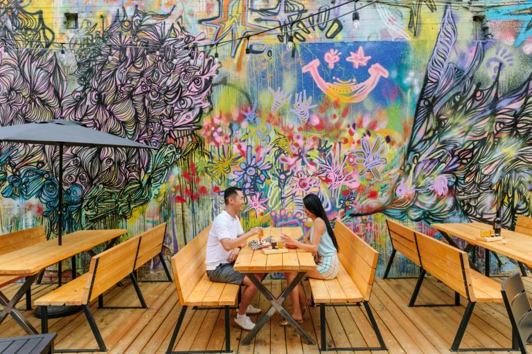 Couple eating lunch next to a colourful street art-inspired mural on a restaurant patio.