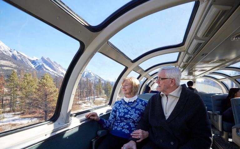 A couple sitting on a train looking out the window to mountains