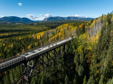 Cyclists ride over the Taunton Trestle with endless forests and a distant mountain range nearby.