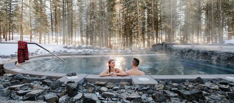 Snow scene with a couple in an outdoor hot tub at the Nordic Spa. Credit: Travel Alberta / Mike Seehagel