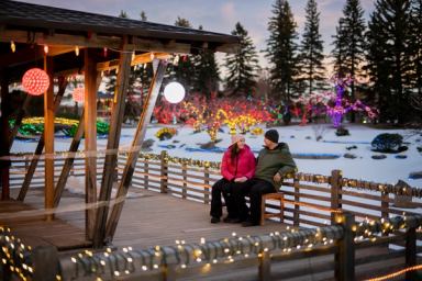 A couple sits outside a Japanese-style building with colourful Christmas lights on trees and plants around them.