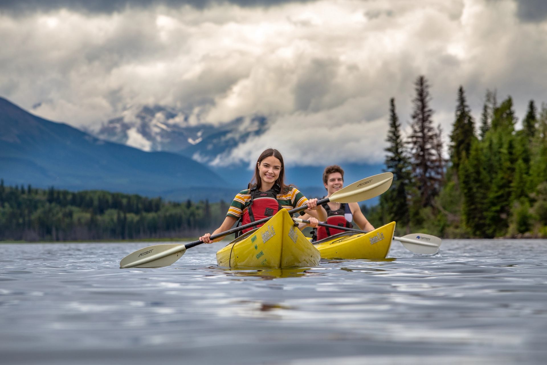 Two kayakers paddle across Grande Cache Lake, surrounded by the Canadian Rockies. 