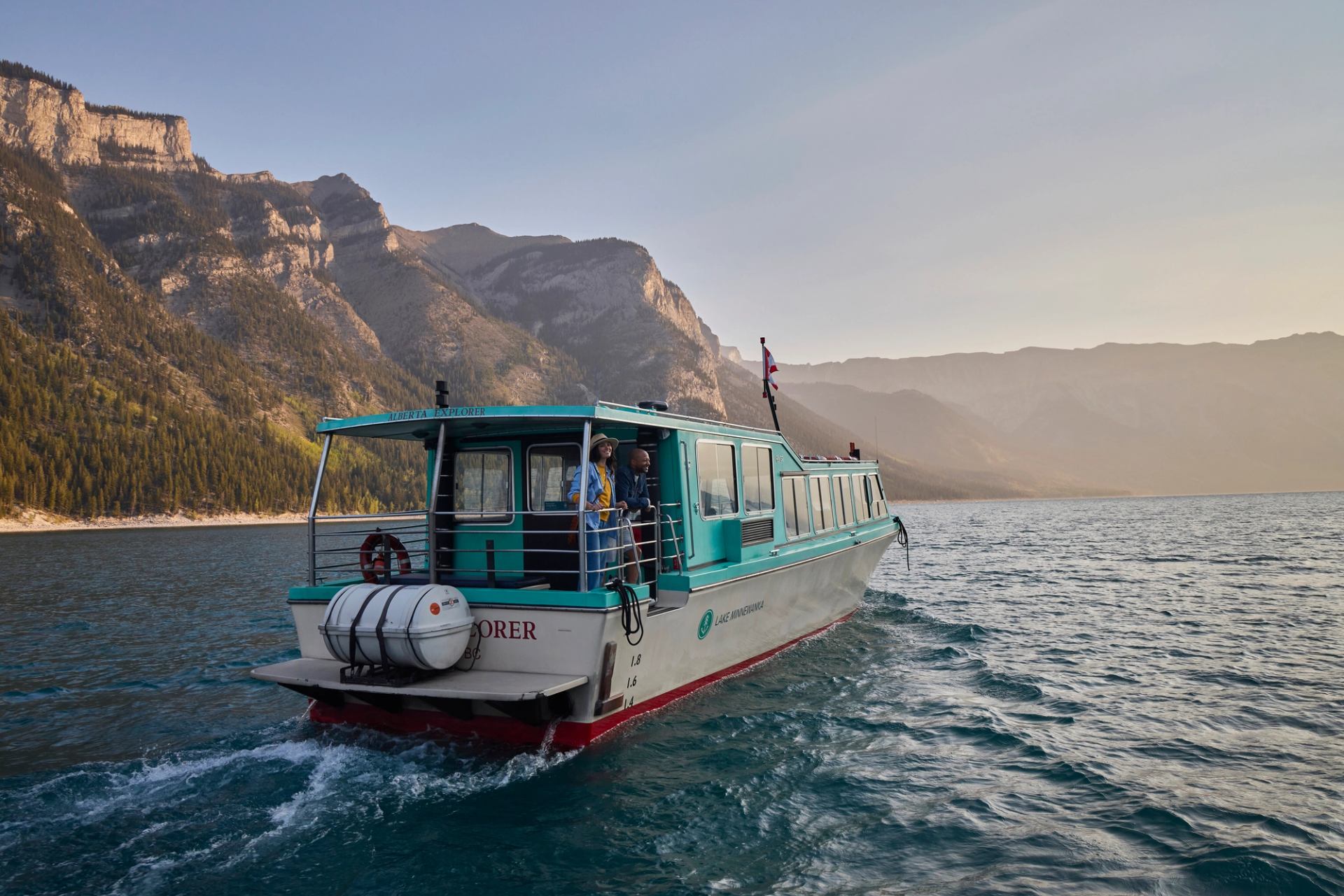 Lake Minnewanka Tour Boat at sunrise, couple looking off back of boat.