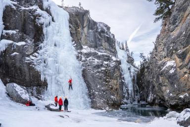 People watch as a climber scales a frozen canyon wall.