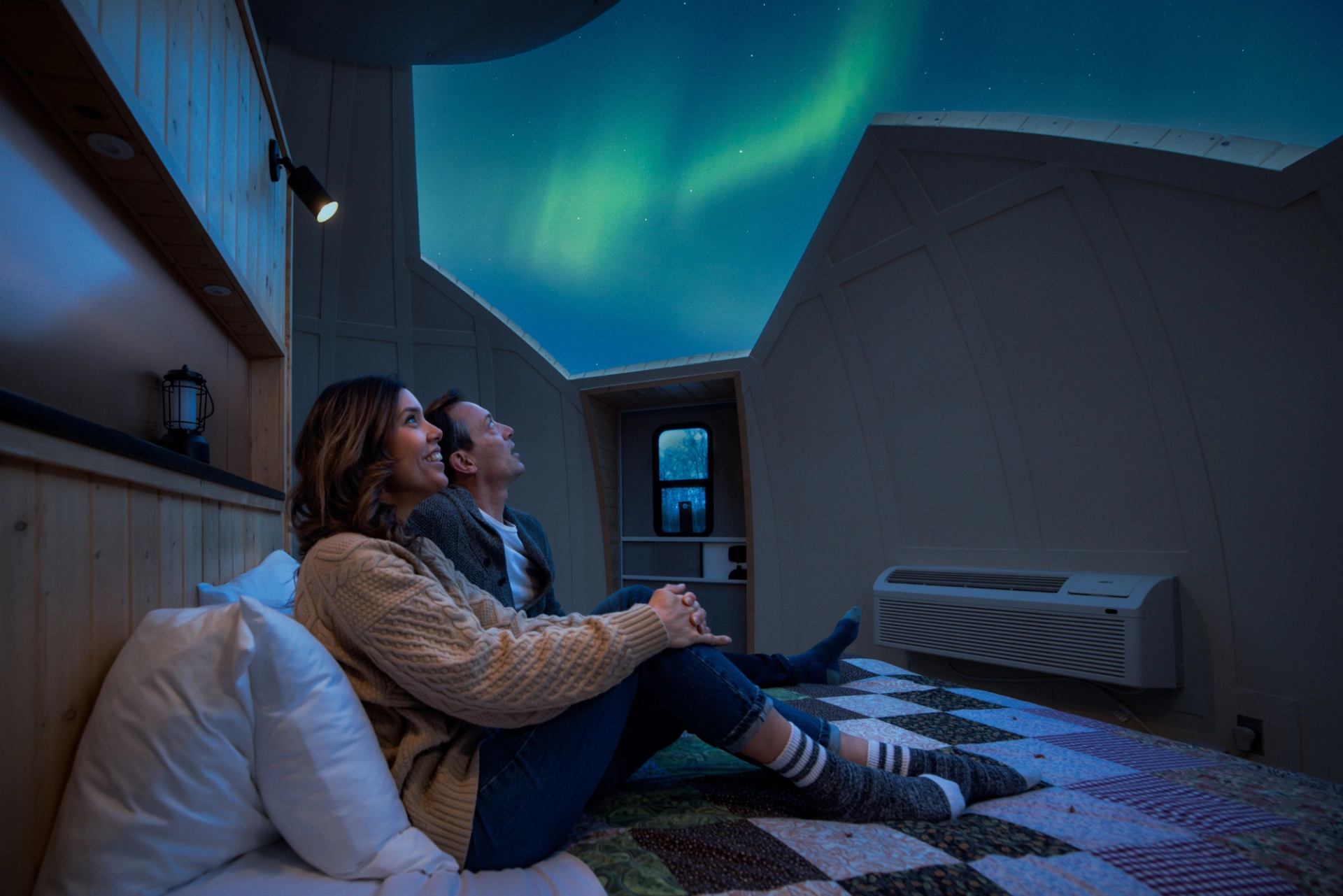 From inside the dome a couple is looking up at the aurora borealis in the night sky