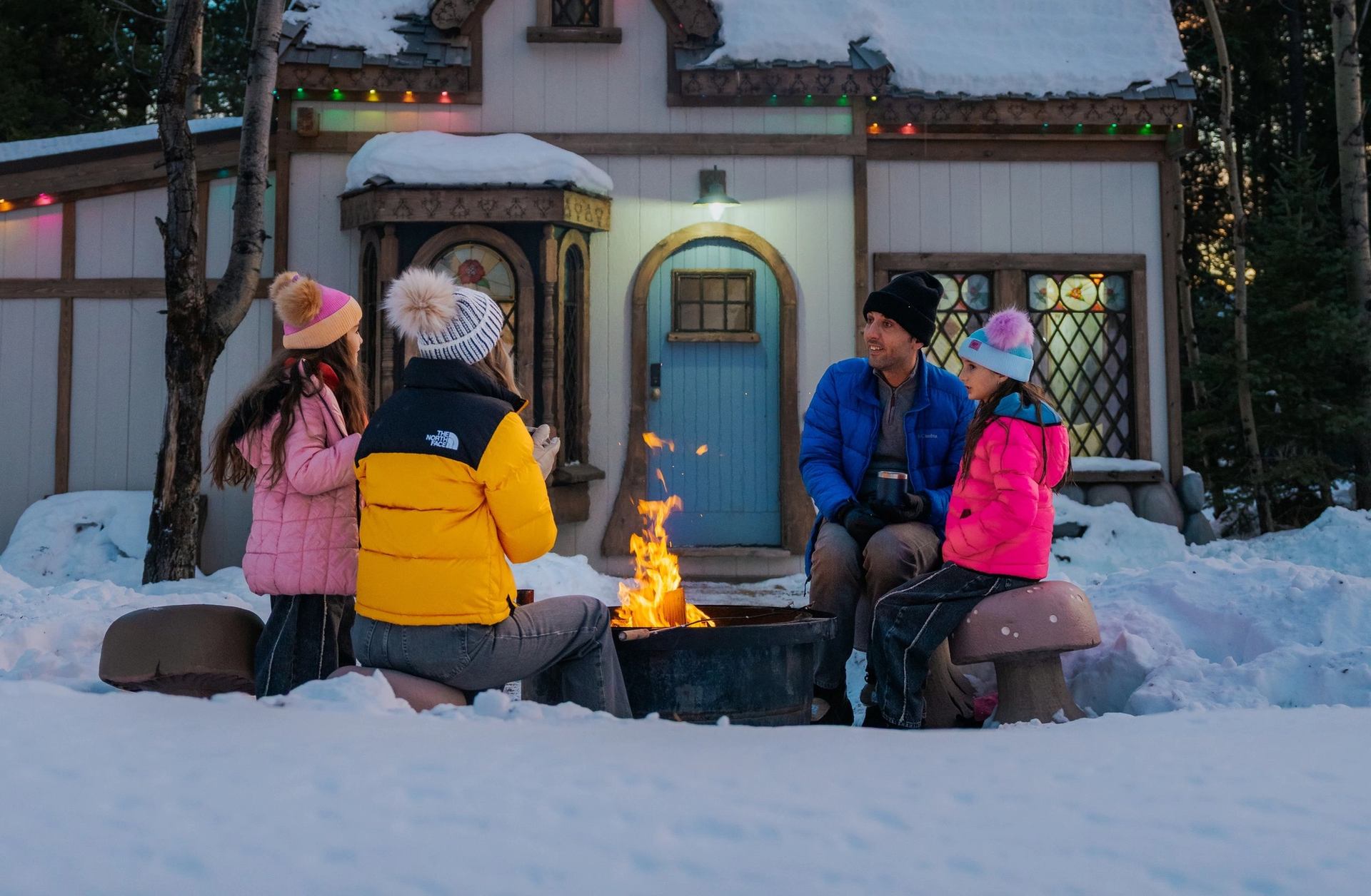 Family sitting around a campfire outside a cottage at Charmed Resorts.