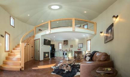 Cozy interior of a grain silo cabin, with spiral stairs to a loft, plus ranch-inspired kitchen and living area.