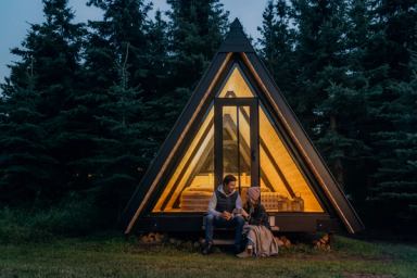 Man and woman sitting on steps of Pine Creek Retreat comfort cabins at dusk.