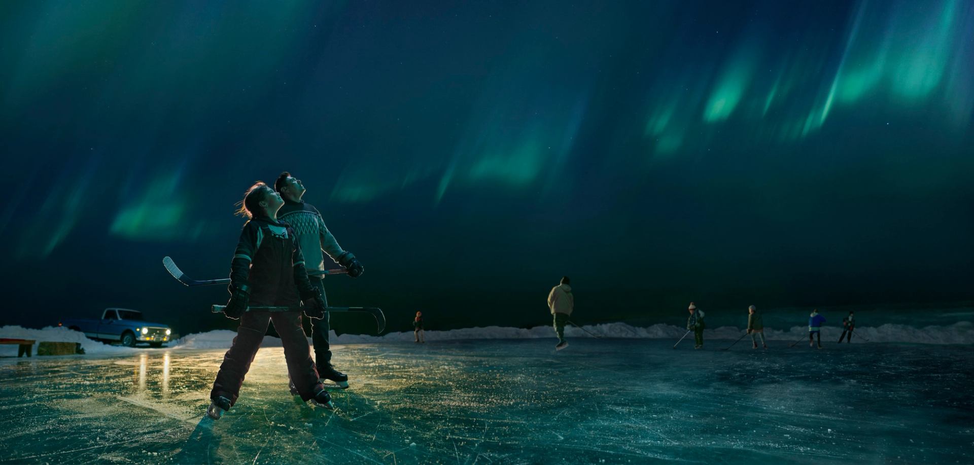 Hockey coach and player pausing from playing pond hockey to look up and admire the Northern Lights overhead.