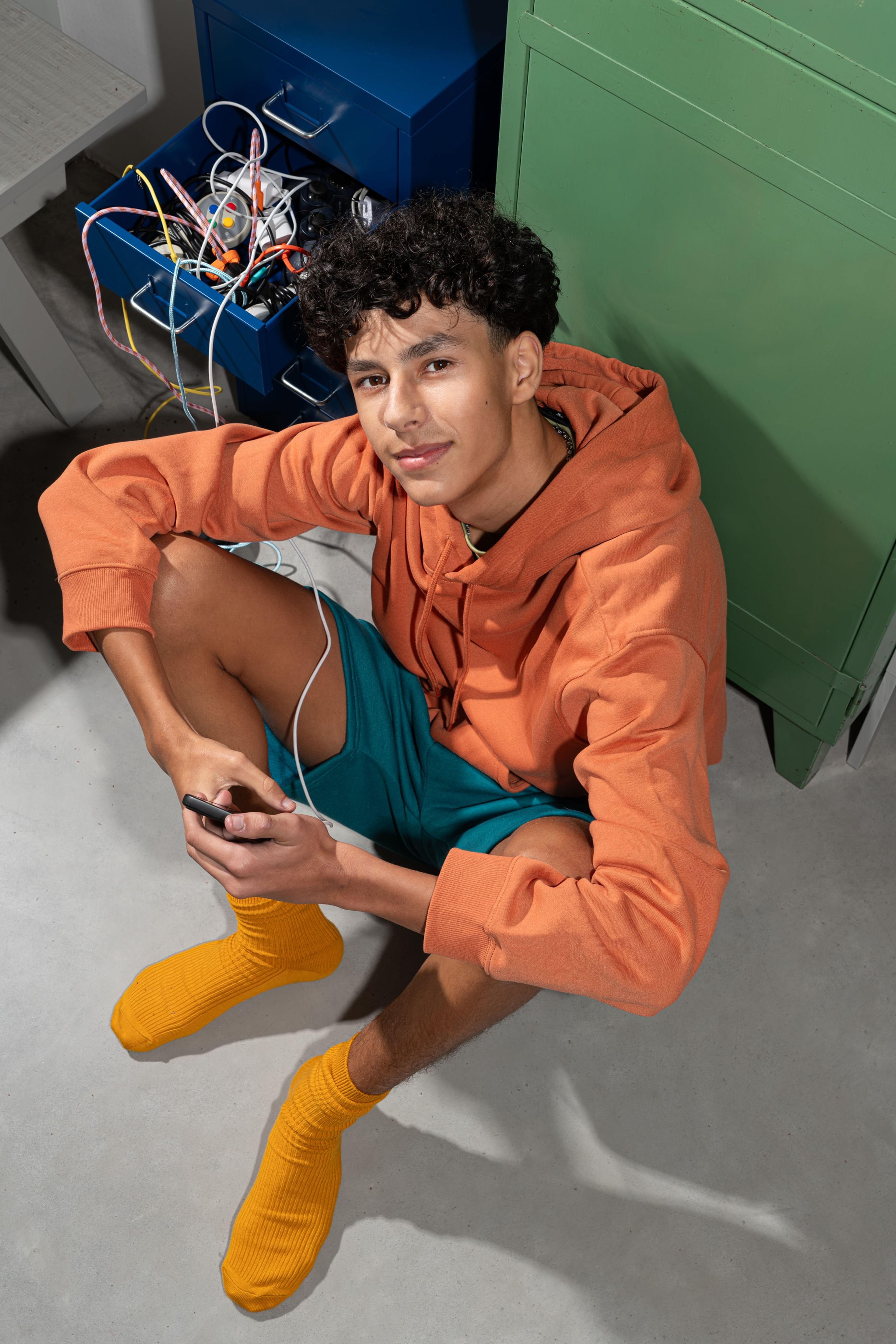 Jongeman laadt zijn telefoon op en zit langs een kast vol kabels en opladers. Goedkope energie verbruiken is nog nooit zo leuk geweest.