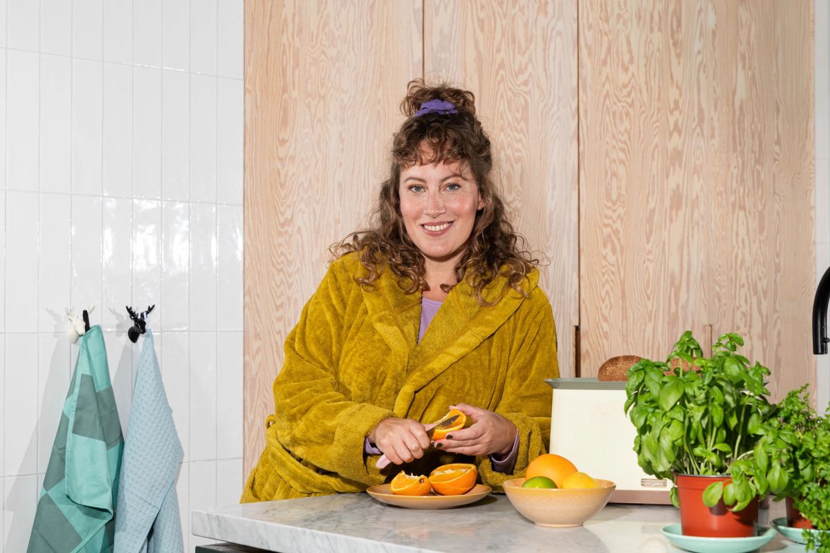 Vrouw schilt een sinaasappel in de keuken, geniet van een rustmoment in een energiezuinig huis.