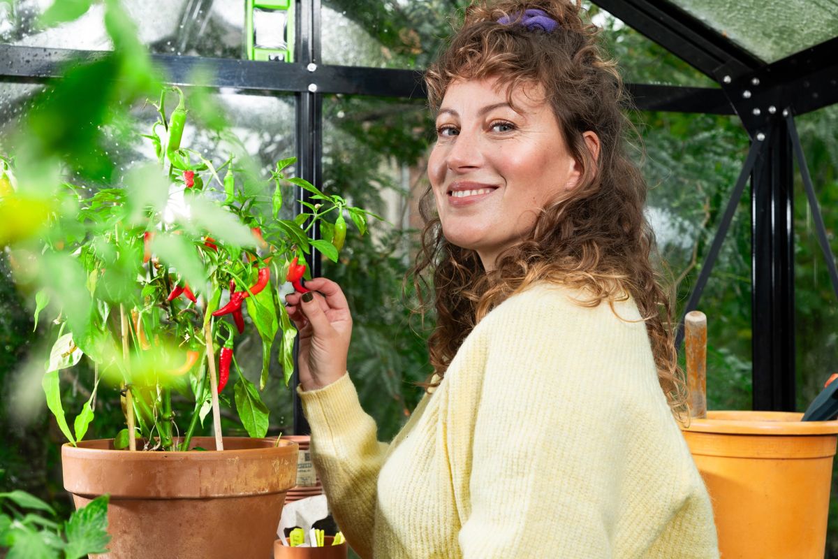 Vrouw met een grote glimlach is haar groenten in een kas aan het bewonderen.