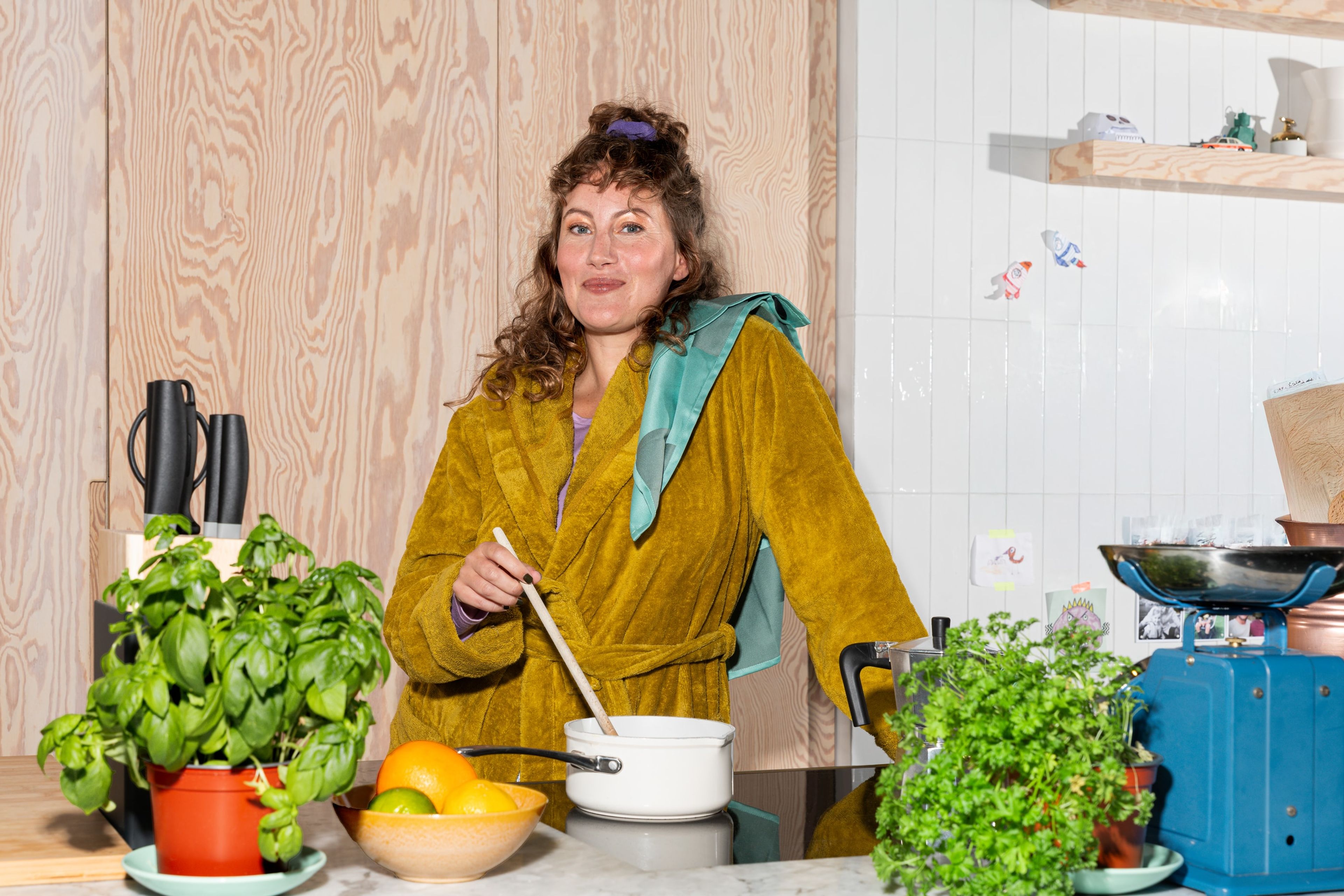 Vrouw roert in een kookpot met kruiden om zich heen, symbool voor bewust energiegebruik in huis.