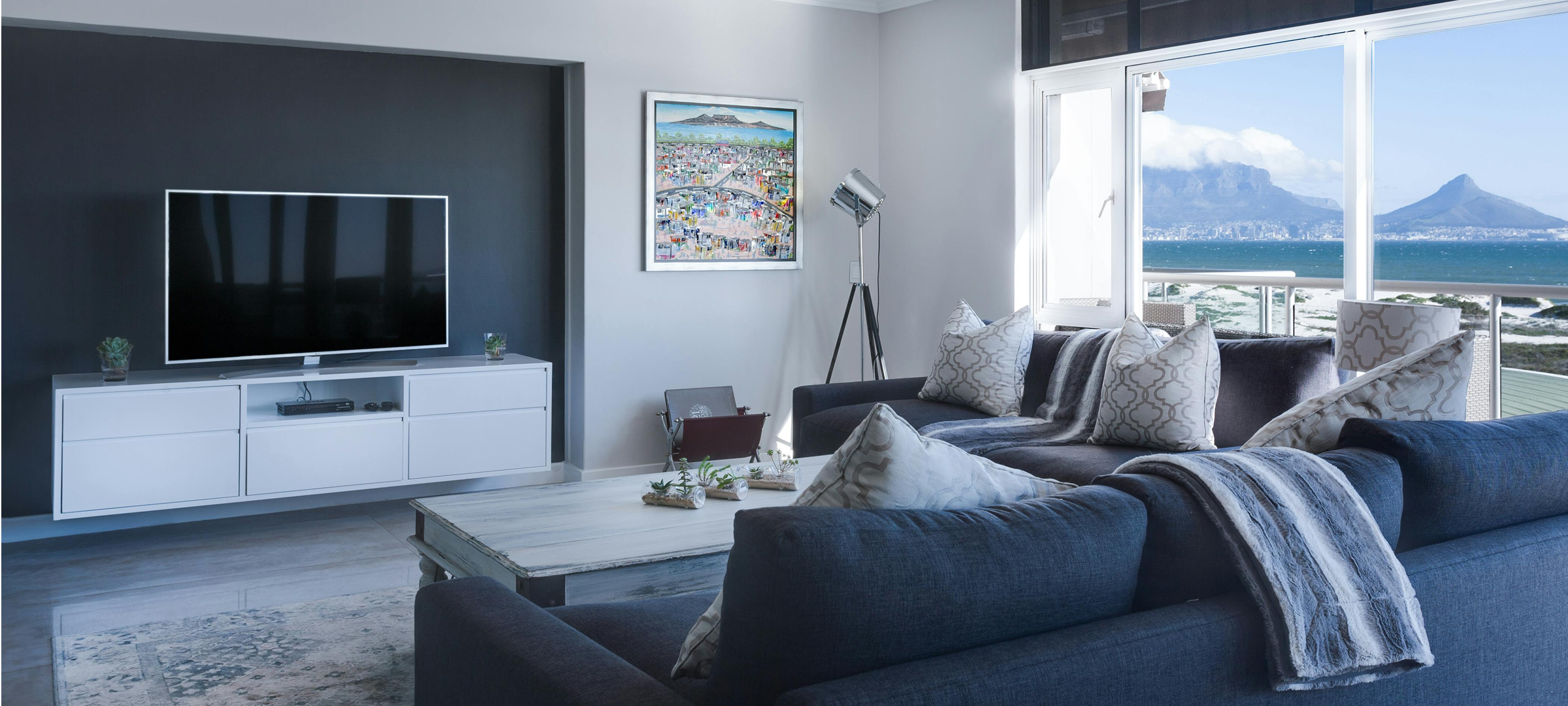 "Luxury Cape Town living room with blue sectional sofa, bespoke media unit, and panoramic Table Mountain ocean views"