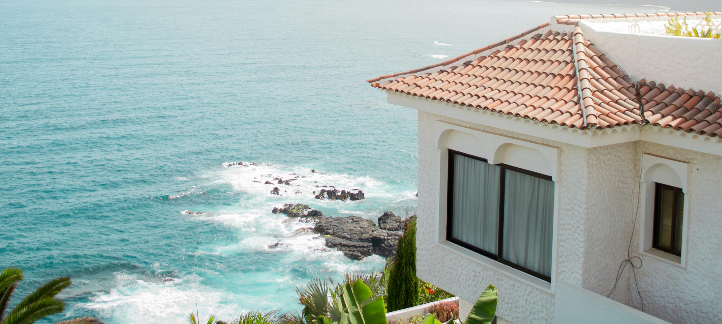 "Luxury coastal beach house with terracotta roof and lush tropical landscaping overlooking turquoise ocean and cliffs"
