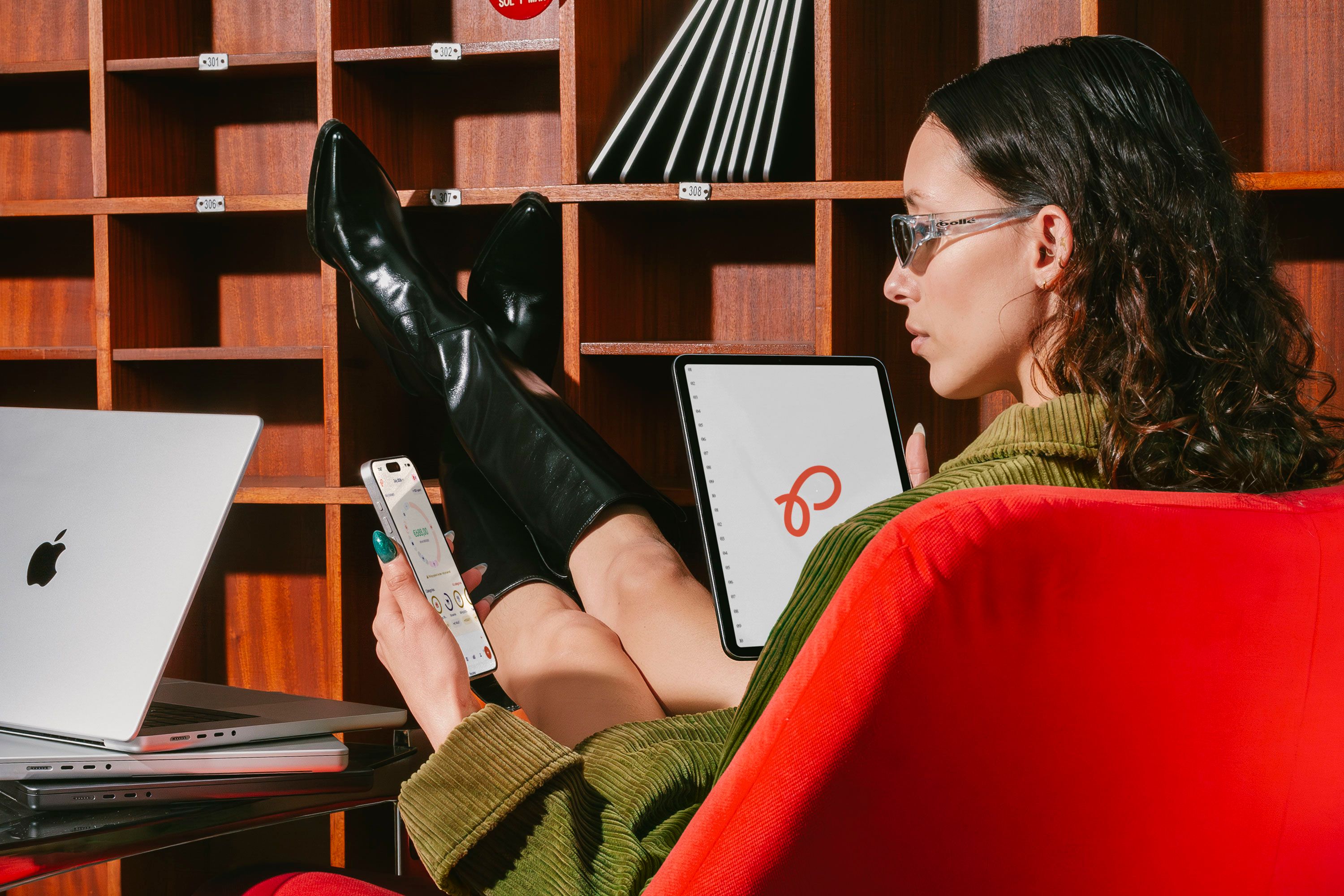 Someone sitting back in a red armchair with their boots up on a shelf, checking the shared budget on their phone.