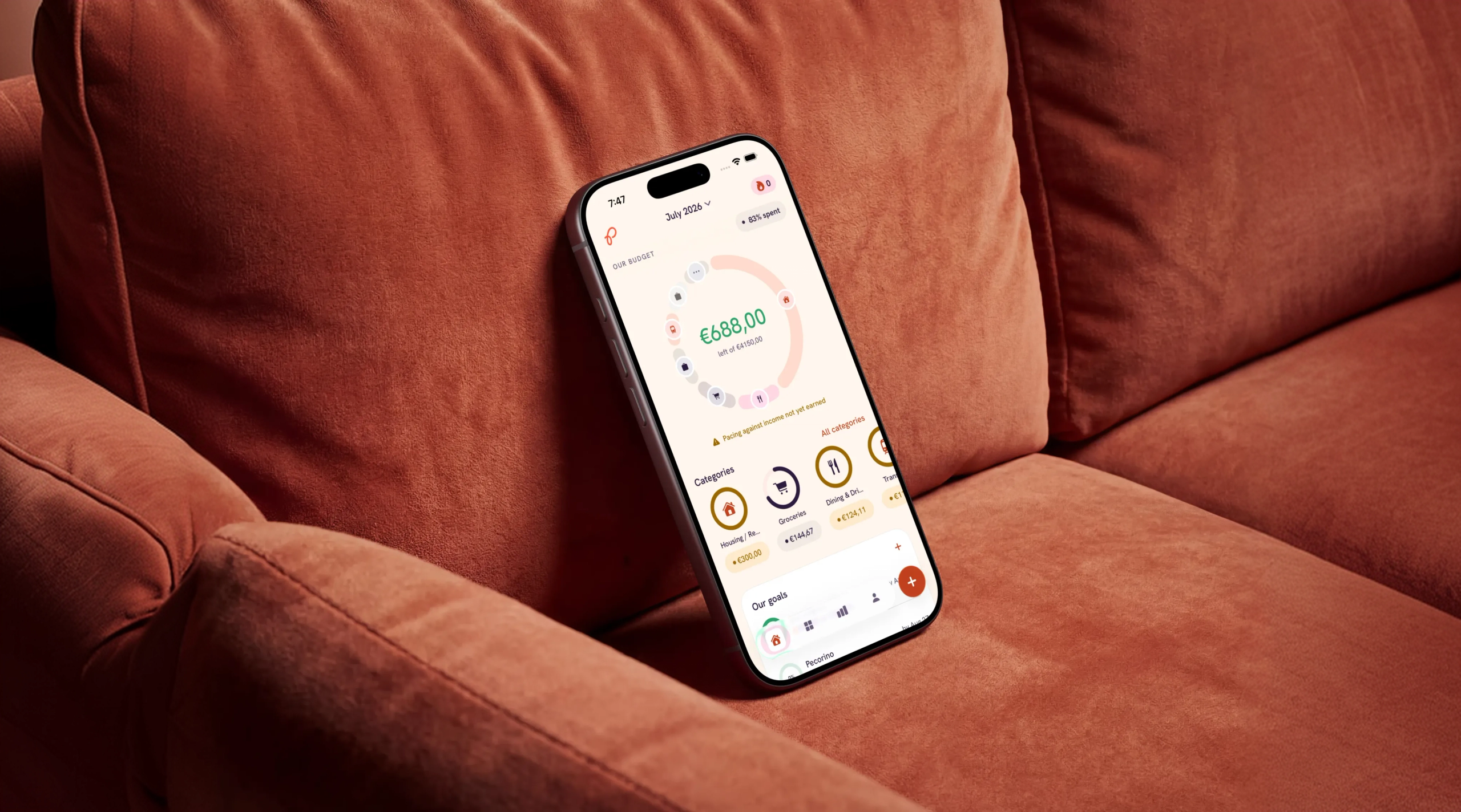 A phone propped on a rust-coloured sofa, showing the month at a glance: €688 still safe to spend out of €4,150.
