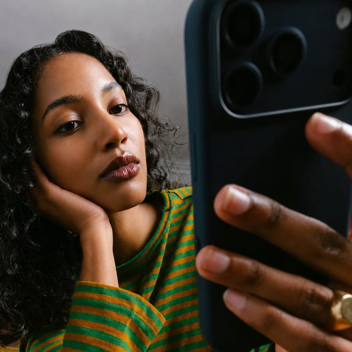 A woman rests her chin on her hand while reading something on her phone.